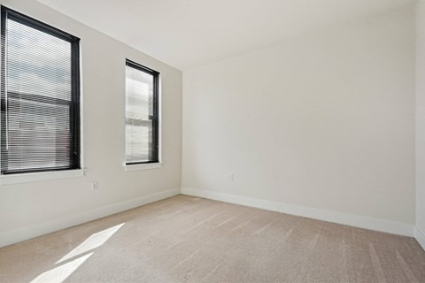 A room with a carpeted floor and two windows.
