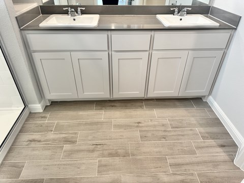 A bathroom with two sinks and grey cabinets.