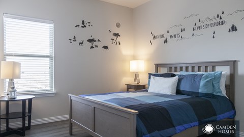 A bedroom with a bed, two lamps, and a wall decal that says "Never stop exploring".