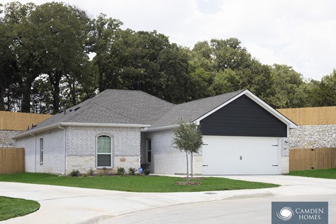 A house with a garage is surrounded by a fence and trees.