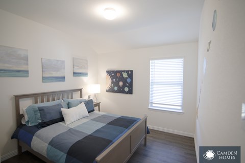 A bedroom with a bed, a window with blinds, and a painting on the wall.