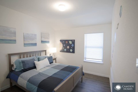 A bedroom with a bed, a window with blinds, and a painting on the wall.
