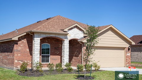 A brick house with a garage door and a sign that says Camden Homes.