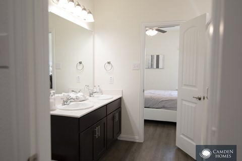 A bathroom with a sink, mirror, and bedroom in the background.