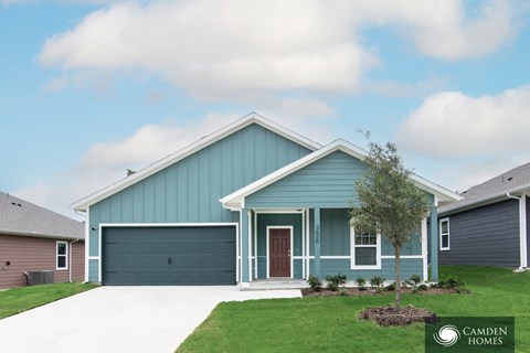 A blue house with a garage door and a tree in front.