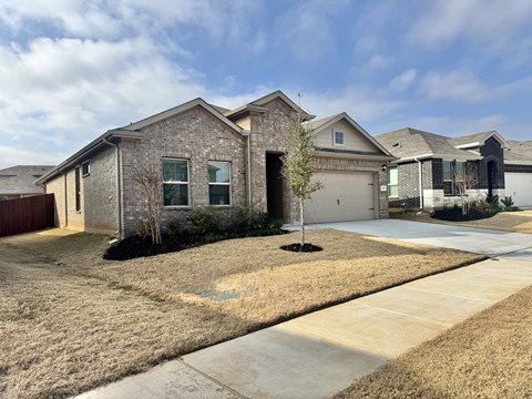 A house with a grey stone exterior and a small tree in front.