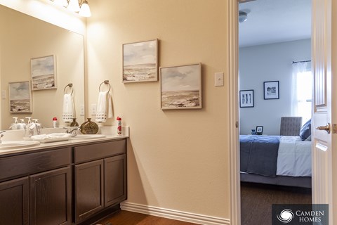 A bathroom with a double sink vanity and a bedroom in the background.