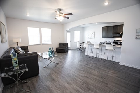 A modern living room with a black couch and a kitchen in the background.