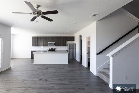 A spacious living room with a ceiling fan and a staircase.