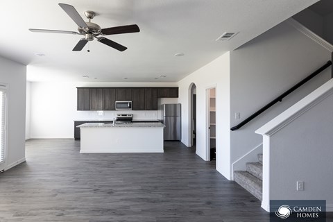 A spacious living room with a ceiling fan and a staircase.
