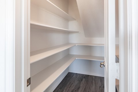 A white pantry with shelves and a wooden floor.