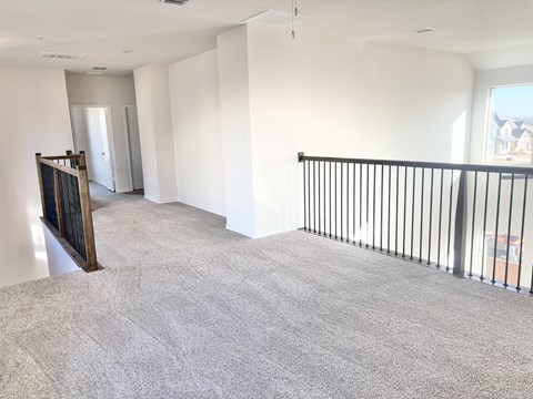 A spacious living room with a grey carpet and a black railing.