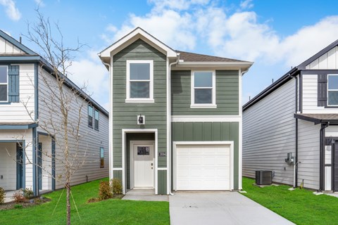 A two-story house with a garage door is in front of other houses.