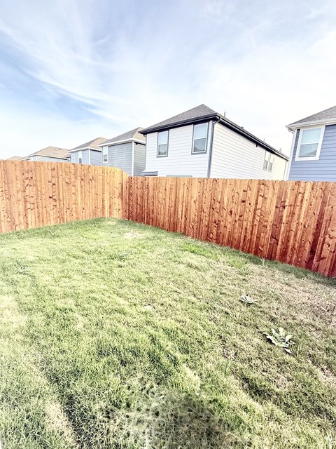 A backyard with a wooden fence and green grass.