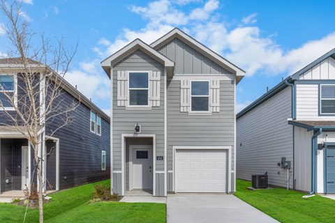 A grey house with a white garage door is in front of a blue house.