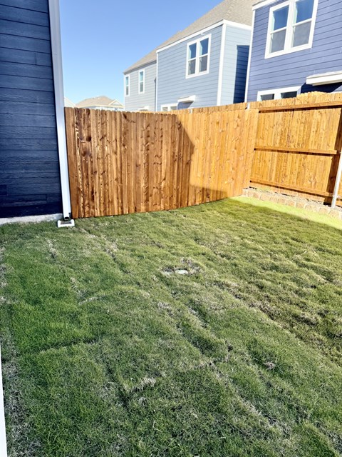A wooden fence separates a green lawn from a blue house.