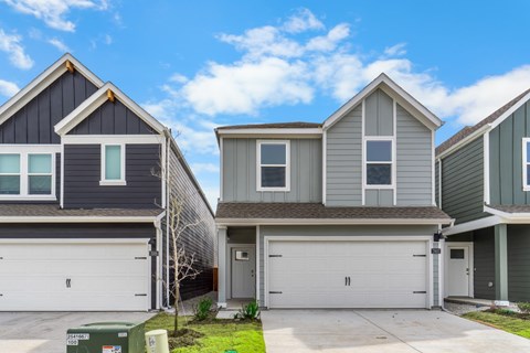 A row of houses with garages and a green trash bin in front of the first house.