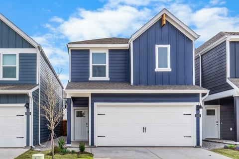 A blue house with a white garage door is in front of two other similar houses.