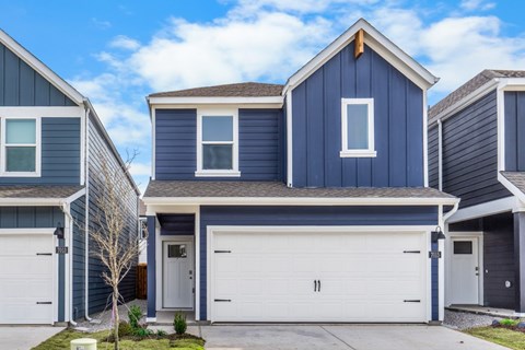 A blue house with a white garage door is in front of two other houses.