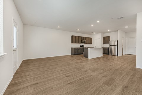 A spacious room with wooden flooring and a kitchen area in the background.