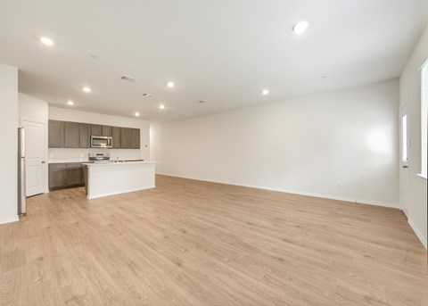 A spacious room with wooden flooring and a kitchenette in the corner.