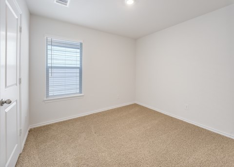 A room with a carpeted floor and a window with blinds.