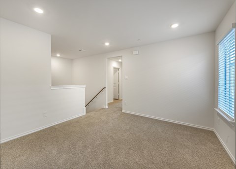 A spacious room with a carpeted floor and a staircase leading to another room.