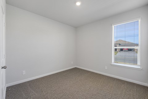 A room with a carpeted floor and a window with blinds.