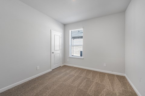 A room with a carpeted floor and a window with blinds.