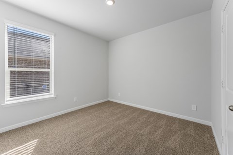 A room with a carpeted floor and a window with blinds.