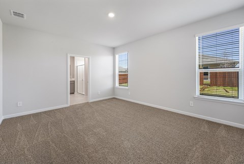 A large empty room with a carpeted floor and a window with blinds.