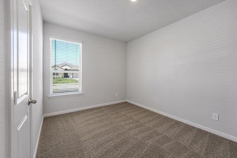 A room with a carpeted floor and a window with blinds.