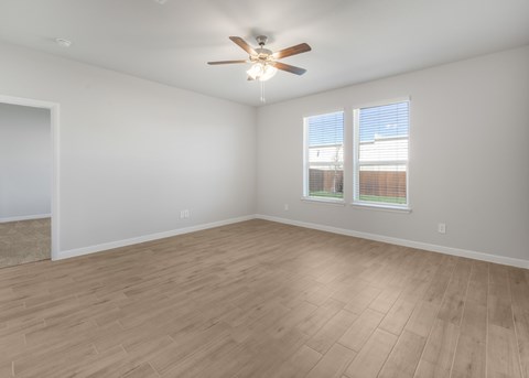 A room with a ceiling fan and light, hardwood floors, and a window with blinds.