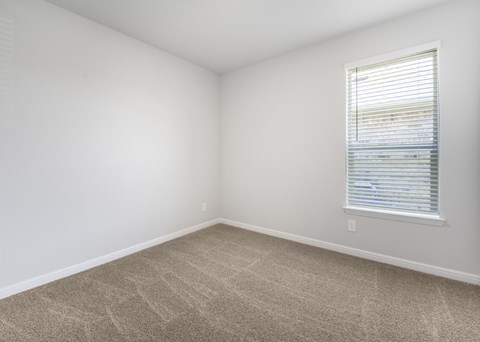 A room with a carpeted floor and a window with blinds.