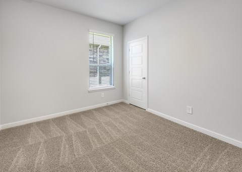 A room with a carpeted floor and a window with blinds.