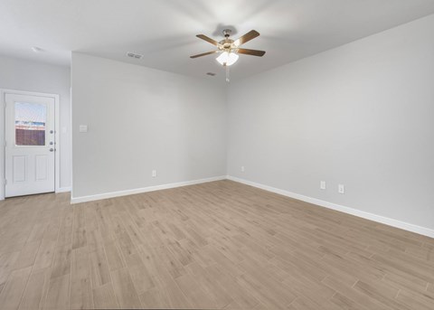 A room with a ceiling fan and light fixture, wooden flooring, and a door with a view of a building outside.