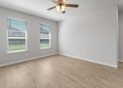 A room with a ceiling fan and two windows.