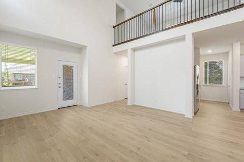 A spacious room with wooden flooring and a balcony with a railing.