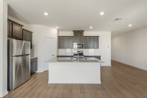 A modern kitchen with a stainless steel refrigerator and wooden flooring.