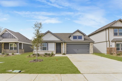 A house with a grey roof and a tree in front of it.