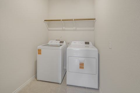 Two white appliances in a room with a shelf above them.