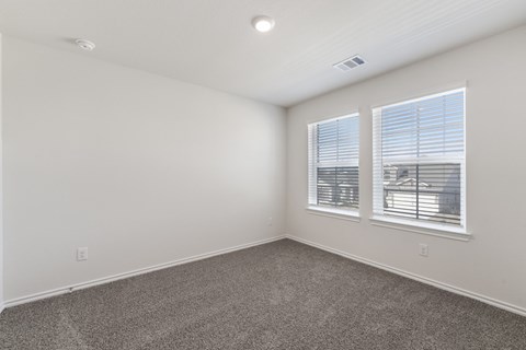 A room with a carpeted floor, two windows with blinds, and a ceiling light fixture.