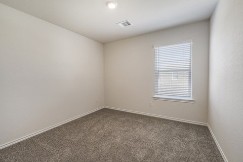 A room with a carpeted floor and a window with blinds.