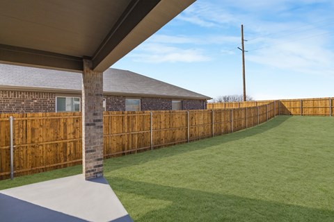 A backyard with a wooden fence and a covered patio area.