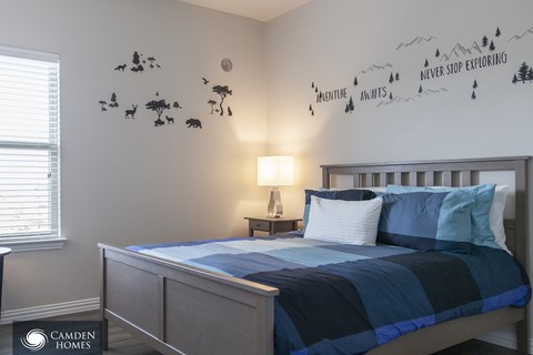 A bedroom with a bed, lamp, and a wall decal that says "Adventure Awaits".