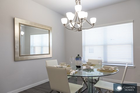A dining room with a glass table and chairs, a chandelier, and a framed mirror on the wall.