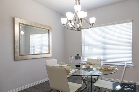 A dining room with a glass table and chairs, a chandelier, and a framed mirror on the wall.