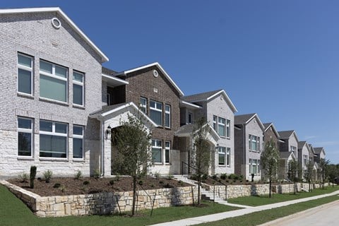 A row of houses with white and brown exteriors are lined up on a street.