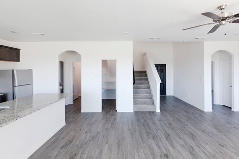 A spacious kitchen with a refrigerator, a staircase, and a ceiling fan.