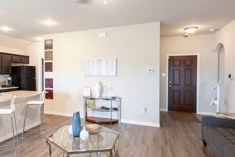 A modern living room with a glass coffee table and a kitchen area in the background.